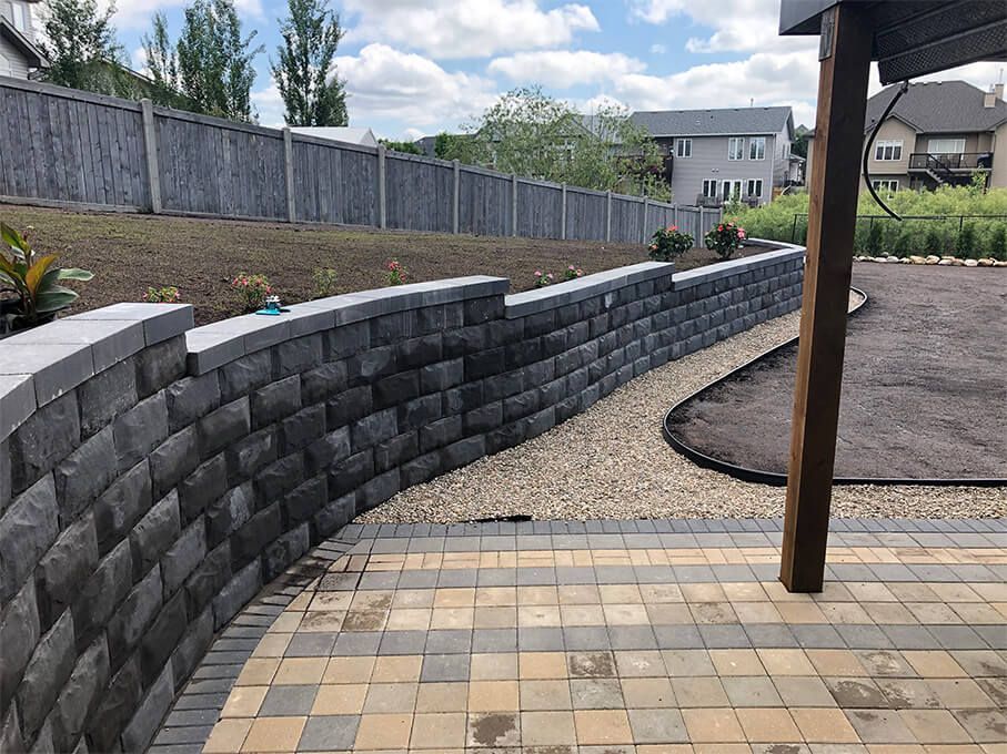A brick wall surrounds a patio in a backyard.