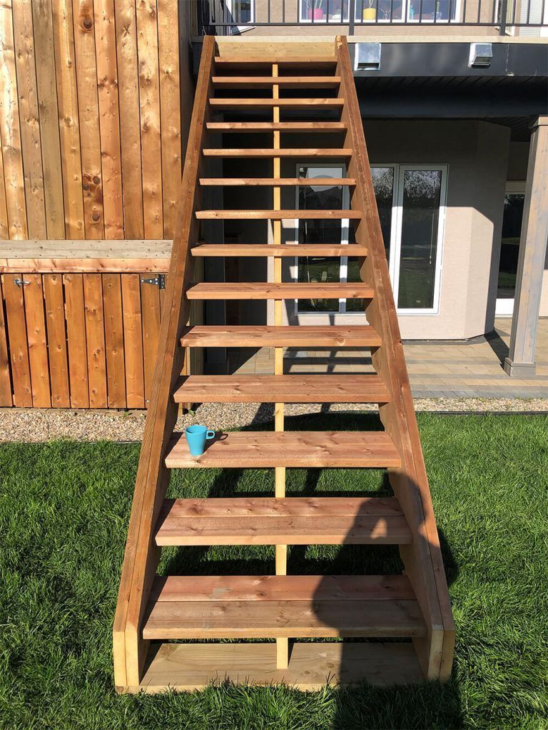 A wooden staircase is sitting in the grass in front of a house.