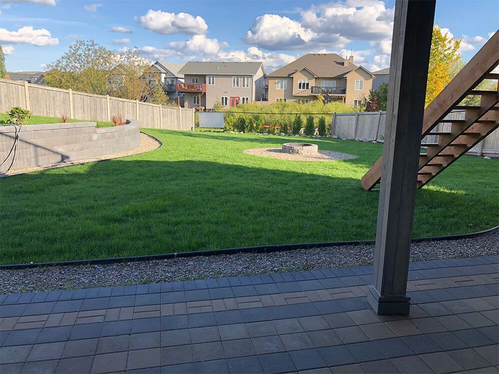 A patio with stairs leading up to a lush green yard with houses in the background.