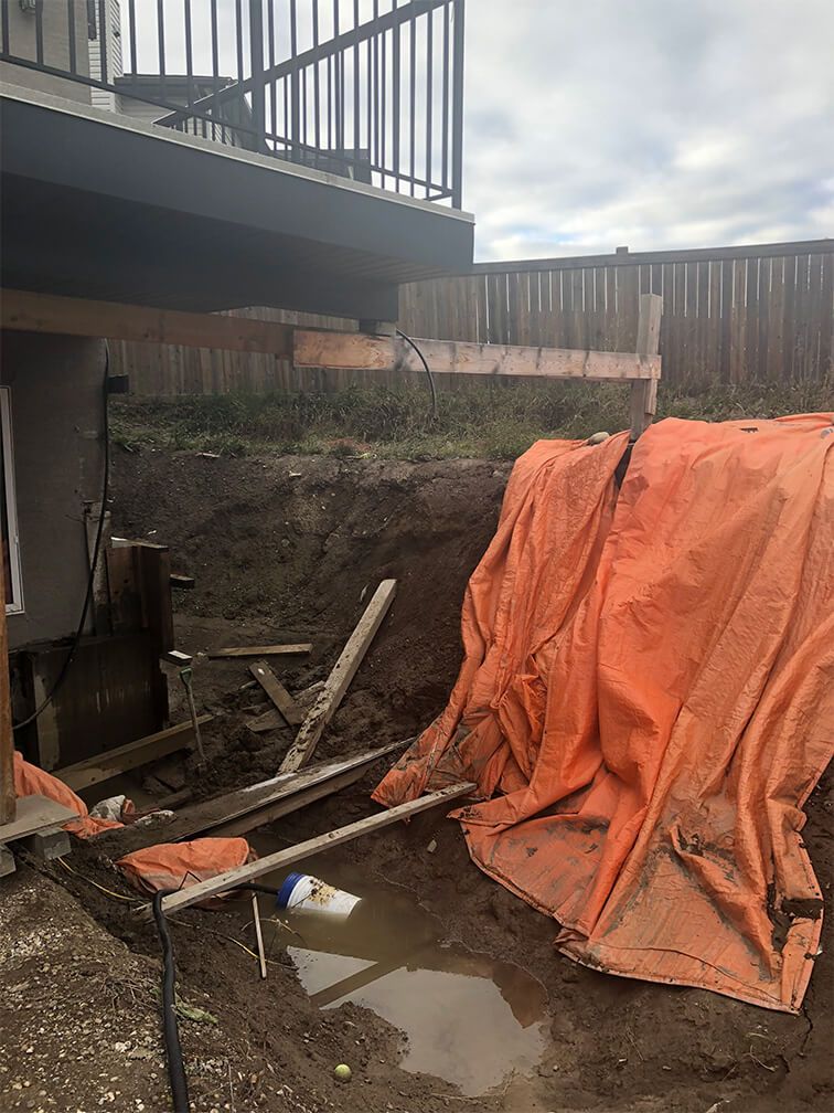 A tarp is covering a hole in the ground in front of a house.