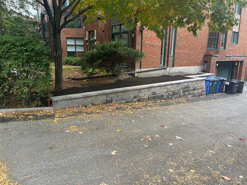 A brick building with a stone wall and trash cans in front of it.