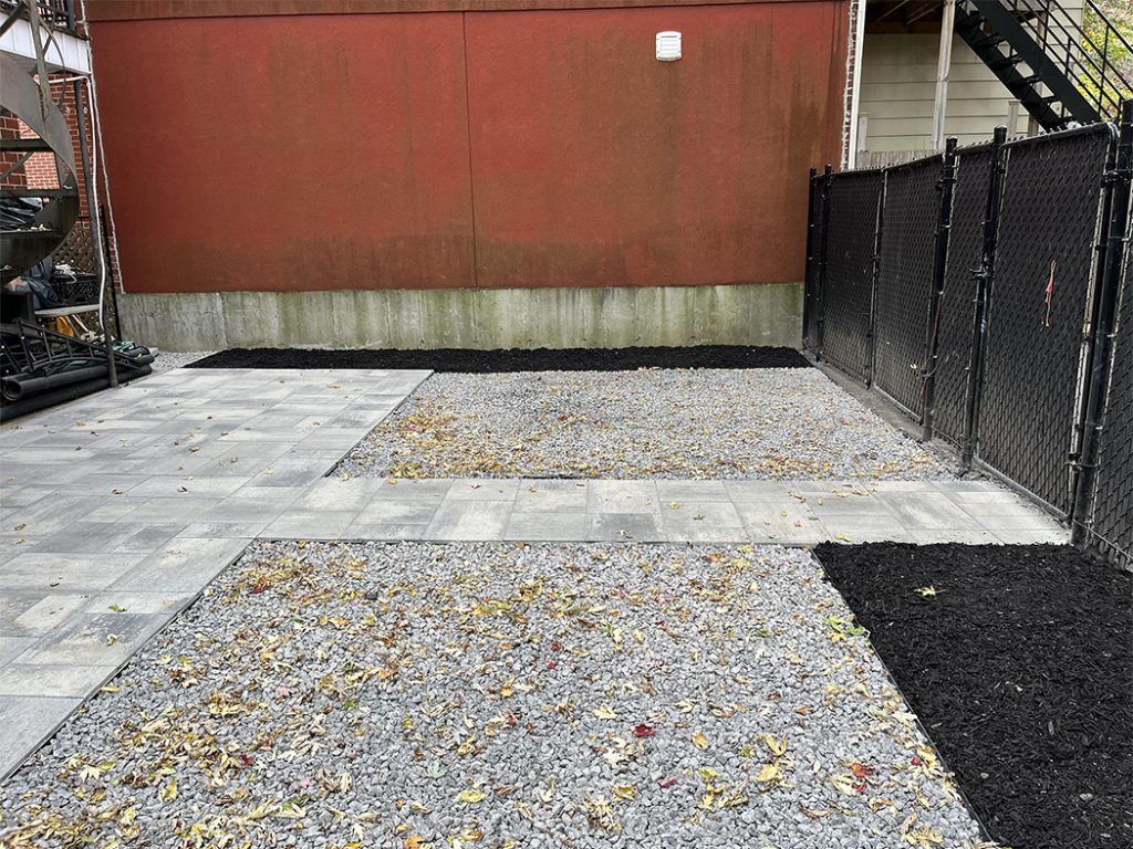 A gravel driveway with a chain link fence and a red wall in the background.