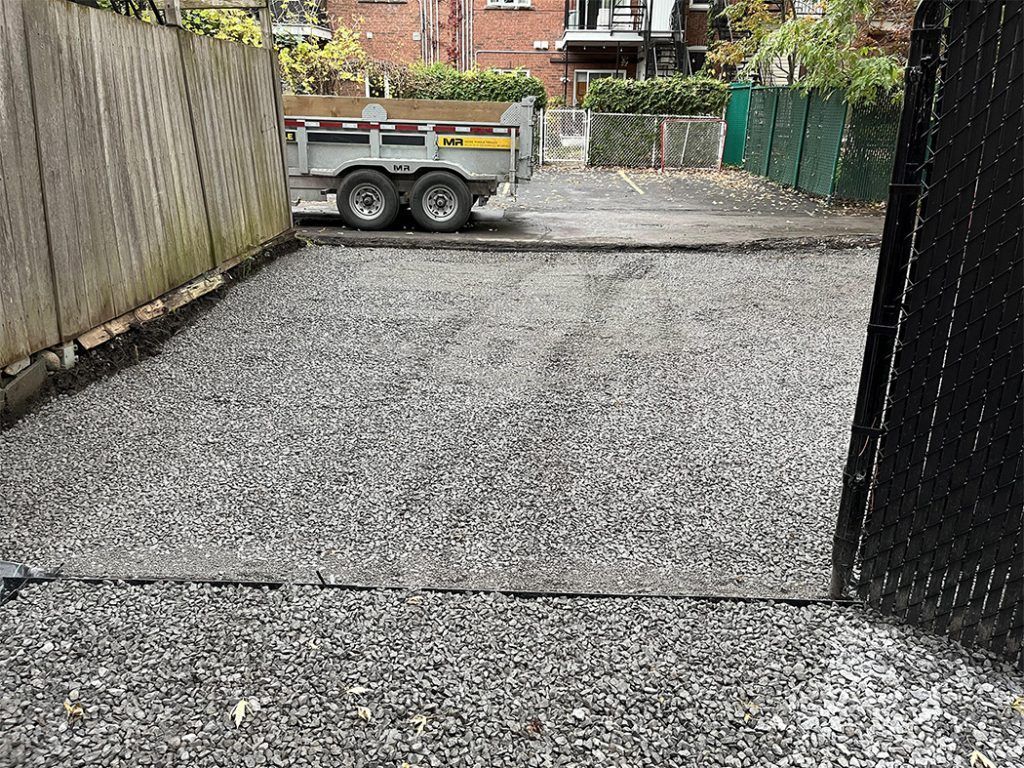 A trailer is parked in a gravel lot next to a fence.