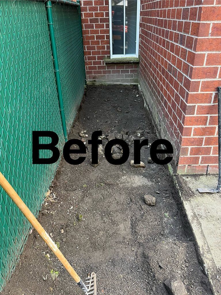 A before picture of a sidewalk with a rake and shovel in front of a brick building.