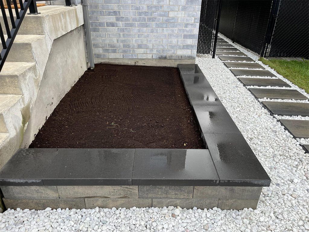 A planter filled with dirt and gravel next to a brick wall.