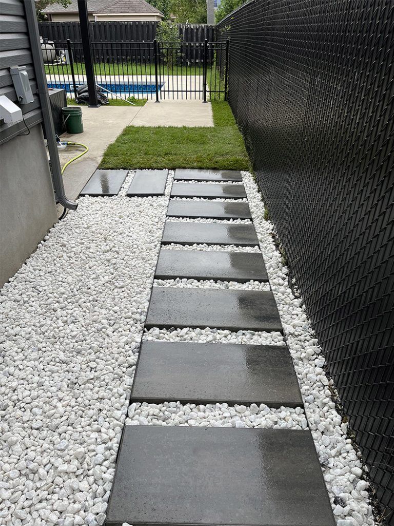 A walkway with black tiles and white gravel leading to a pool.