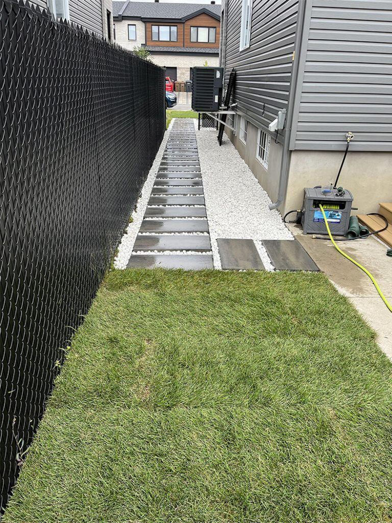 A sidewalk leading to a house with a black chain link fence.