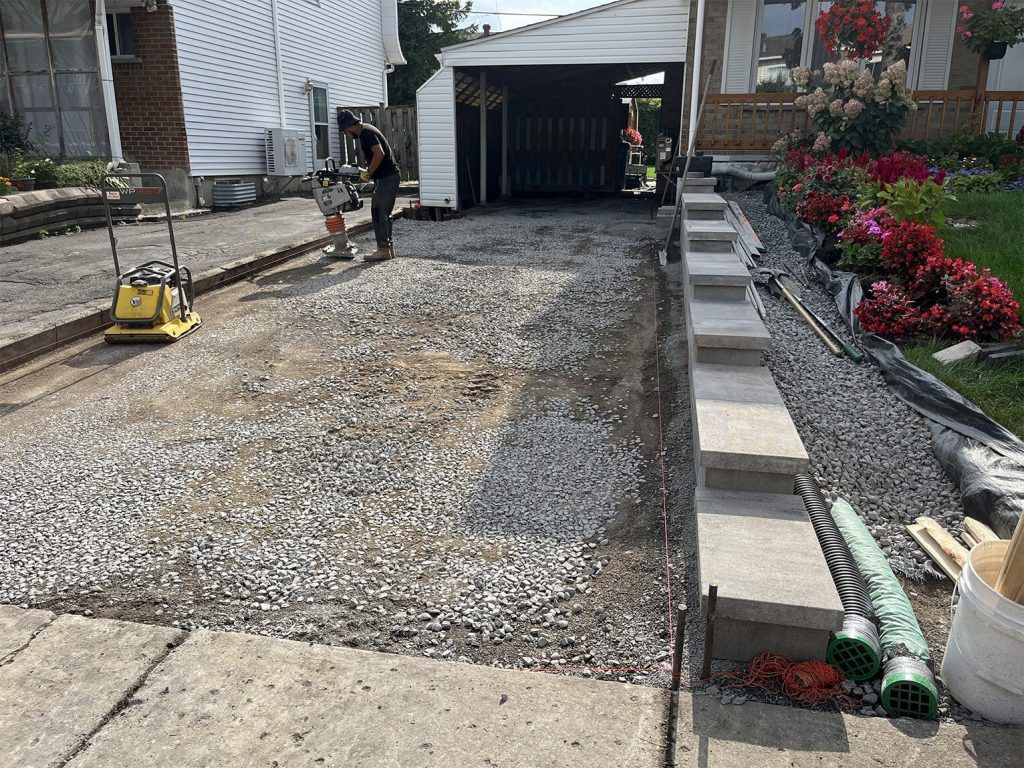 A man is working on a gravel driveway in front of a house.