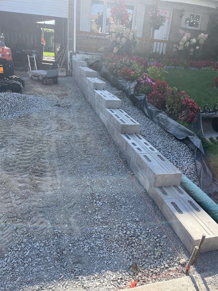 A row of bricks sitting on top of a gravel road in front of a house.