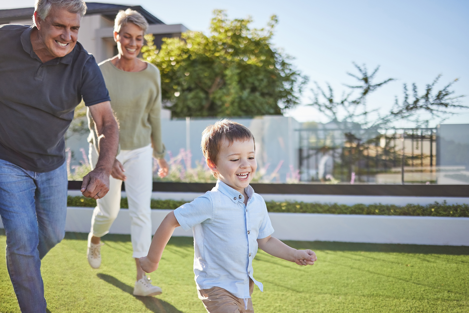 A boy is running towards an elderly couple sitting on a blanket in the grass.