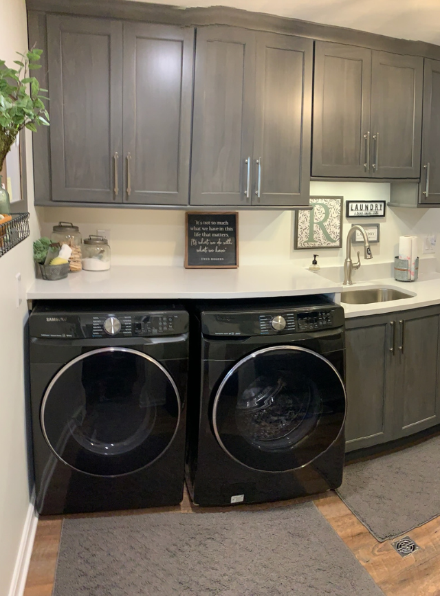 Laundry room with black washer and dryer under gray cabinets and countertop decorations.