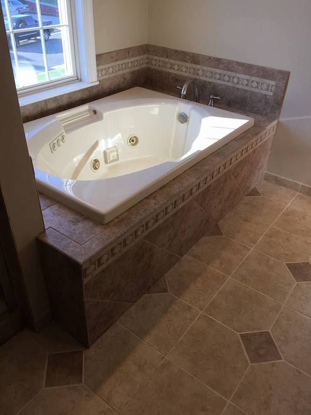 Built-in corner soaking tub with tan tile surround in a bathroom near a window.
