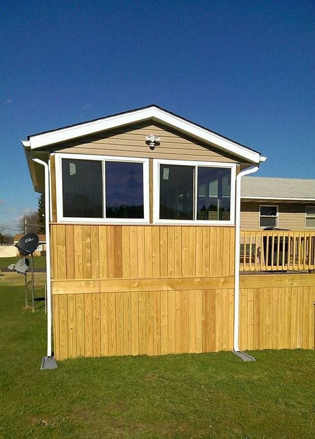 Wooden shed with white-trimmed windows on a grassy lawn under a clear blue sky