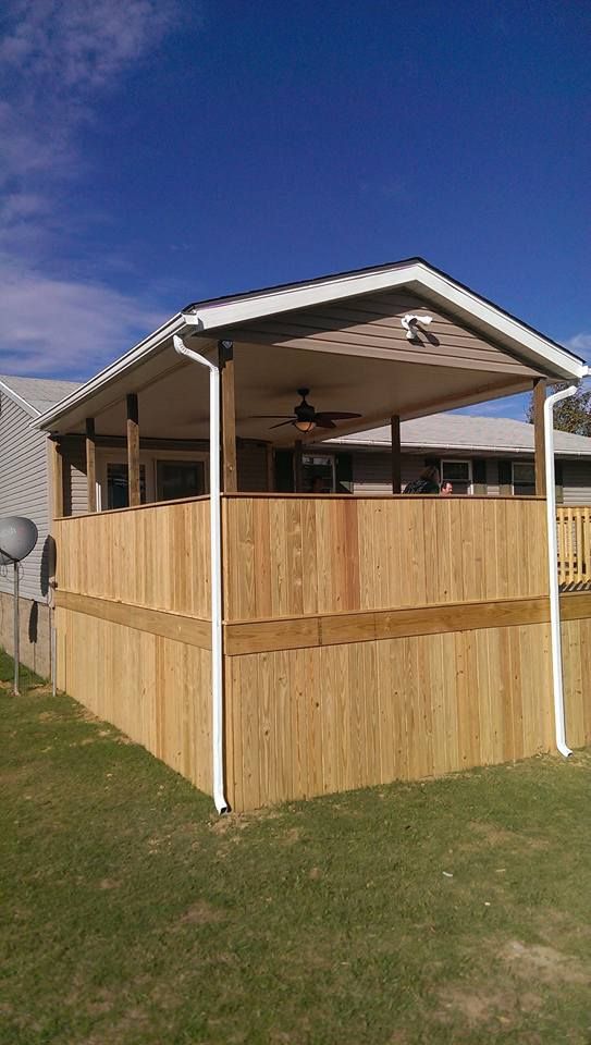 Wooden fenced patio beside a house, with a covered roof and ceiling fan under a blue sky.