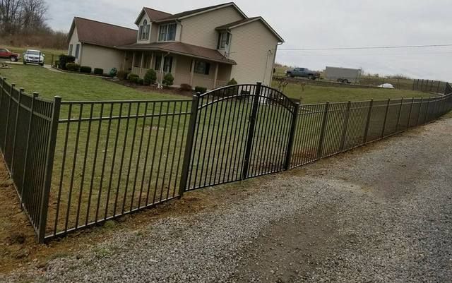 Country house with porch behind a black metal fence beside a gravel road