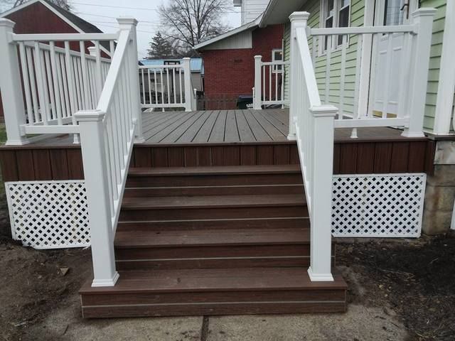Wooden front porch stairs with white railings and lattice skirting, leading to a deck.