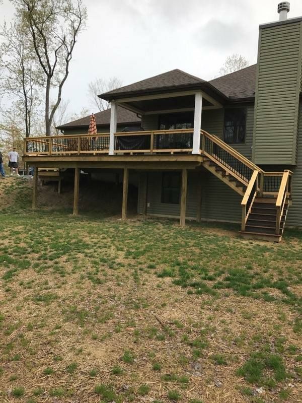 Raised wooden deck with stairs beside a house, overlooking a grassy yard.