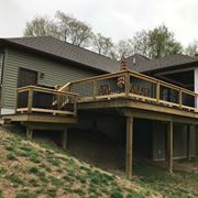 Raised wooden deck on a house, with railings, stairs, and an American flag, overlooking a sloped yard.