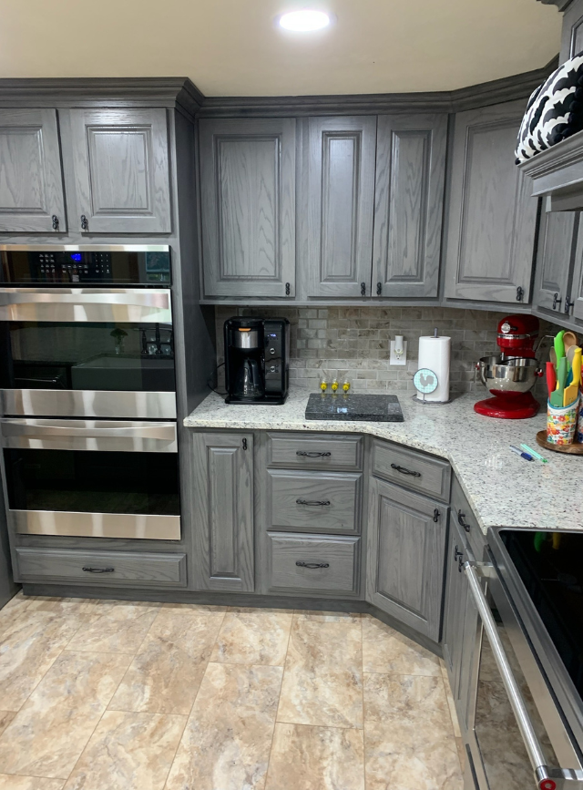 Modern gray kitchen with built-in oven, coffee maker, granite counters, and tile floor