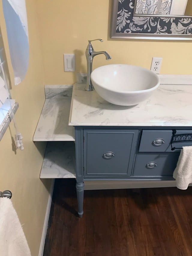Bathroom vanity with white vessel sink, blue cabinet, and towel shelf beside a window and wood floor