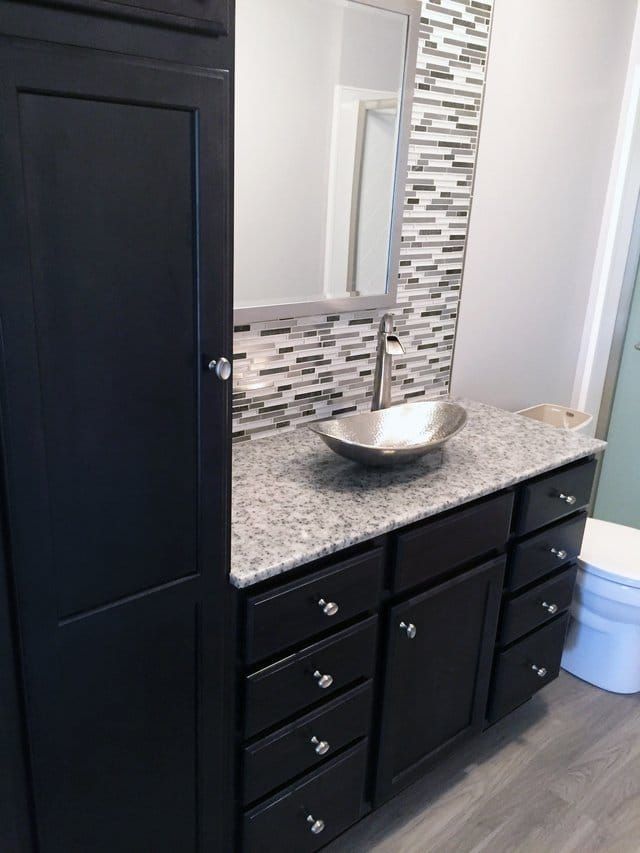 Bathroom vanity with black cabinets, speckled countertop, bowl sink, and mosaic tile backsplash