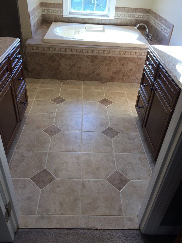 Bathroom with beige tile floor, built-in soaking tub, and patterned tile trim by a window.