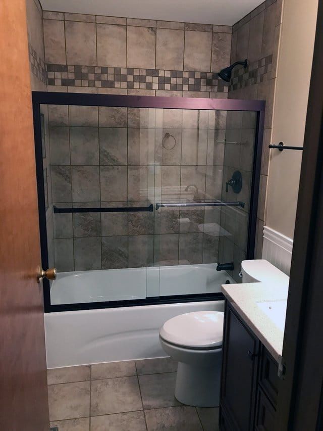 Bathroom with glass shower enclosure, toilet, and vanity sink in gray tile