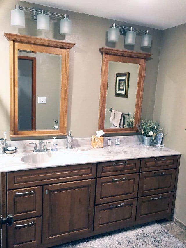 Double vanity bathroom with dark wood cabinets, white countertop, and two mirrors over a speckled floor.