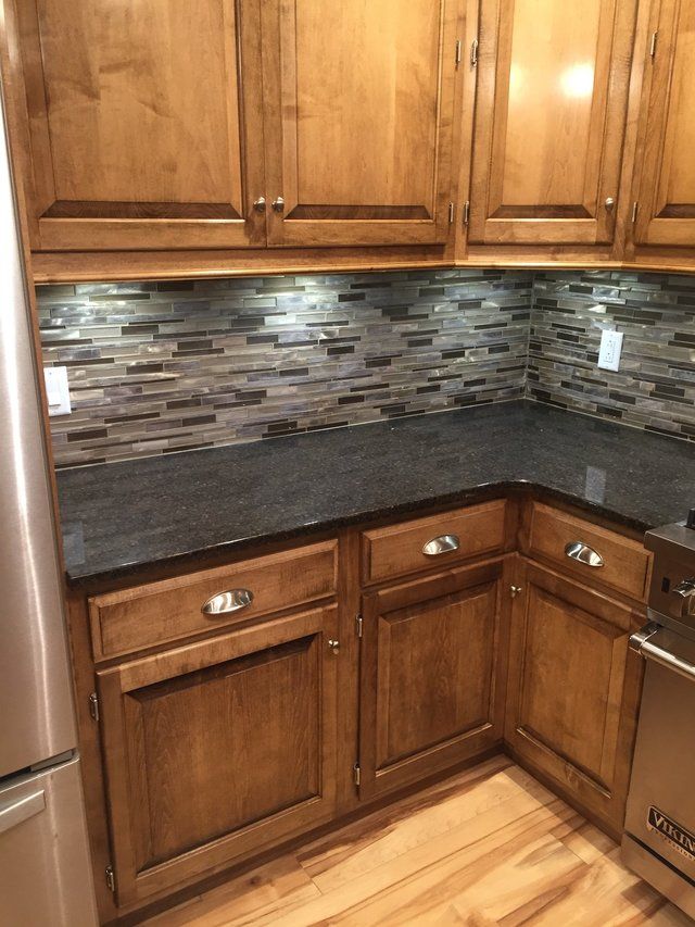 Corner kitchen with wood cabinets, dark countertop, and mosaic tile backsplash