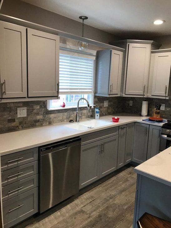 Modern kitchen with gray cabinets, stainless appliances, window over sink, and white countertops