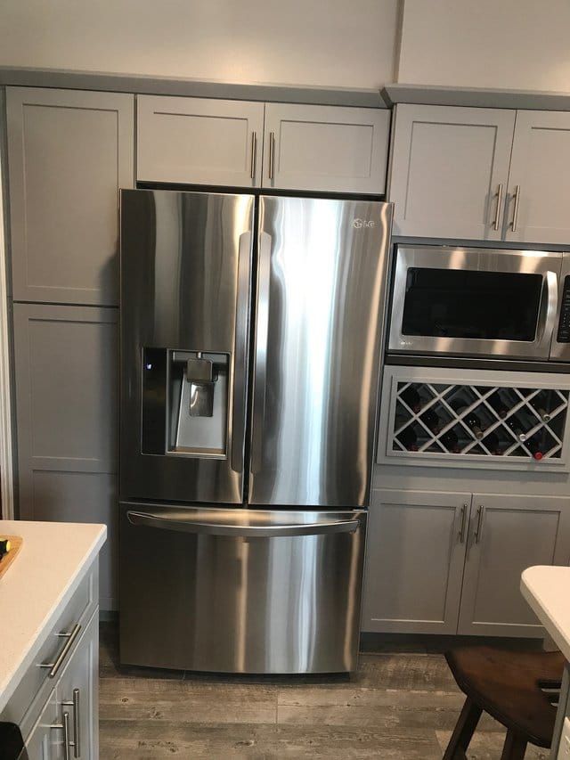 Stainless steel refrigerator in a modern kitchen with white cabinets and built-in microwave.