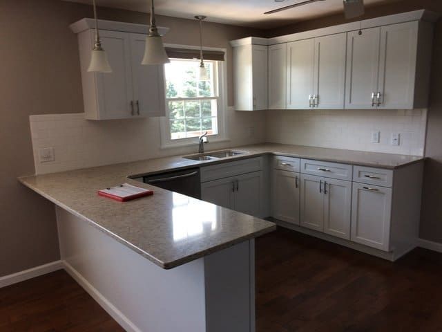 Empty modern kitchen with white cabinets, granite counters, pendant lights, and a window above the sink.