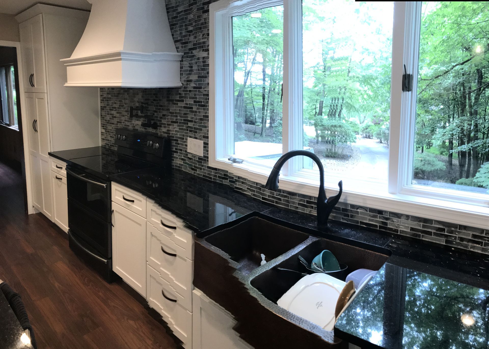 Modern kitchen with black countertops, white cabinets, farmhouse sink, and large window overlooking greenery