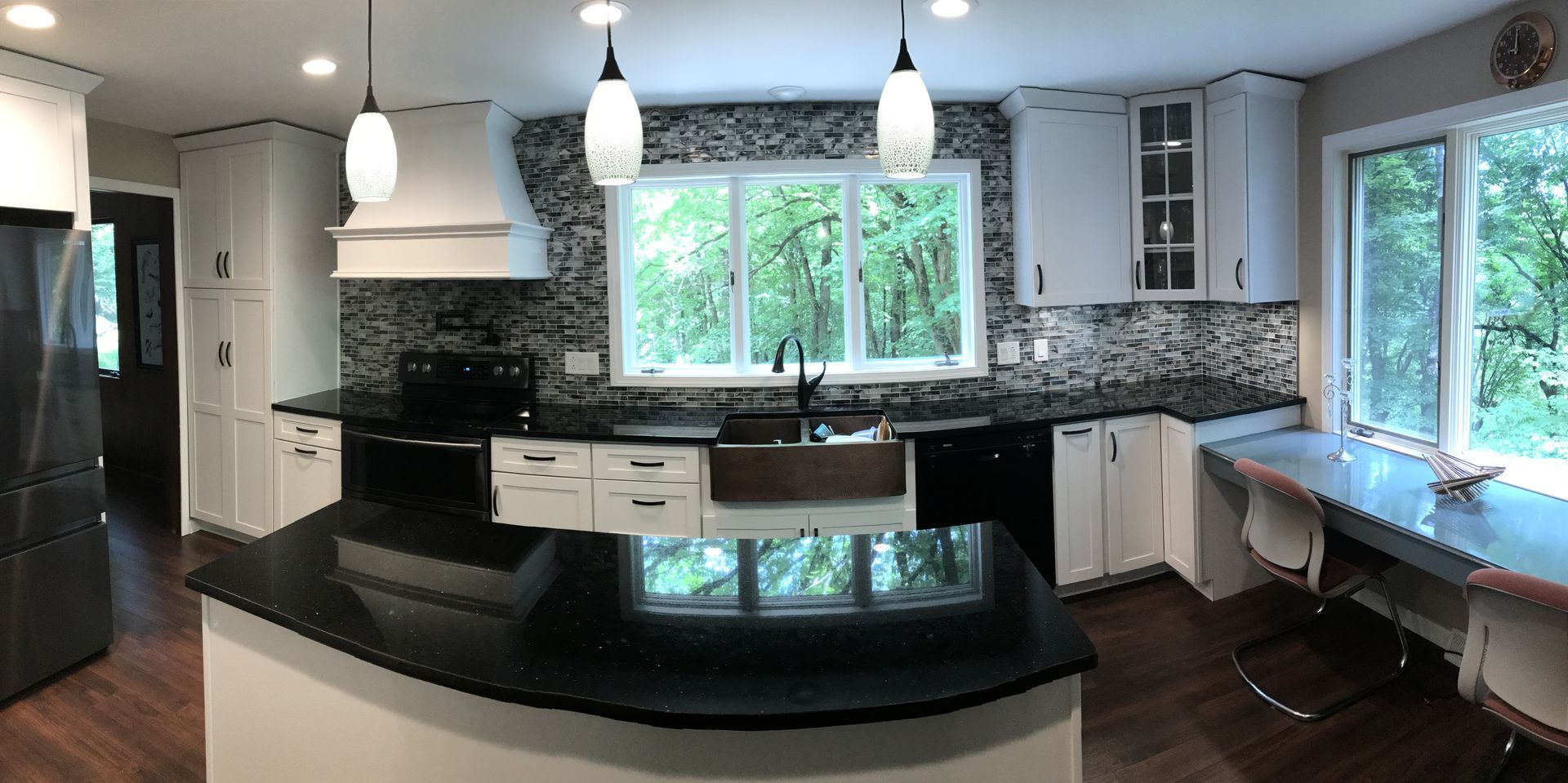 Modern kitchen with black countertops, white cabinets, hanging lights, and large windows