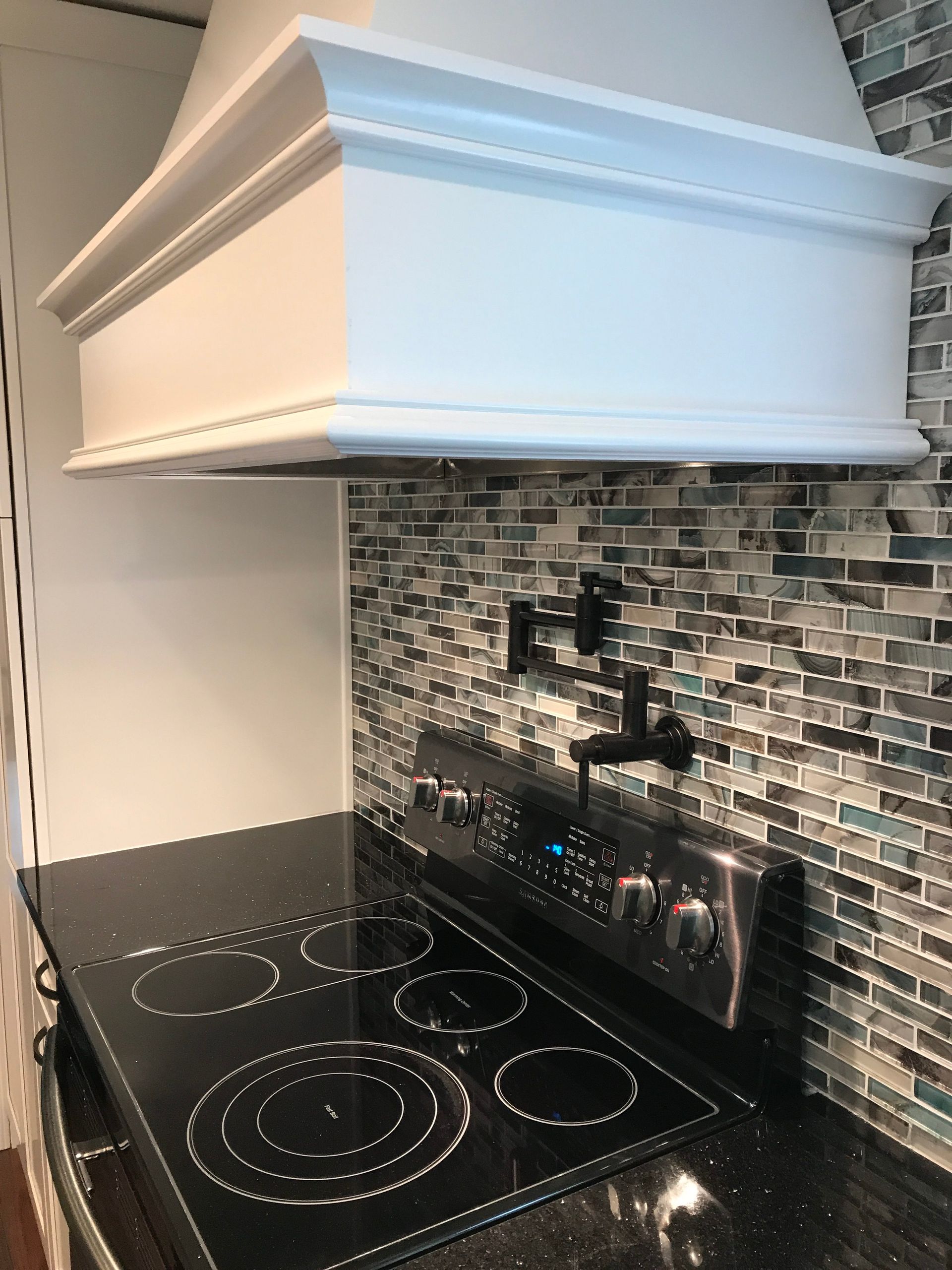 Modern kitchen stove with black glass cooktop, mosaic tile backsplash, and white range hood