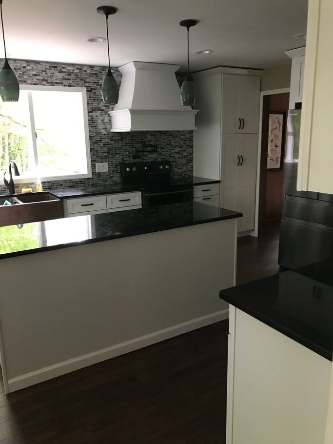 Modern kitchen with black countertops, white cabinets, tiled backsplash, and a window over the sink.