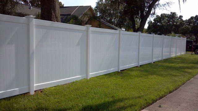 White vinyl privacy fence along a grassy residential yard beside a sidewalk.
