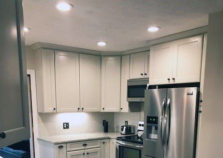 Modern kitchen with white cabinets, stainless steel appliances, and recessed ceiling lights