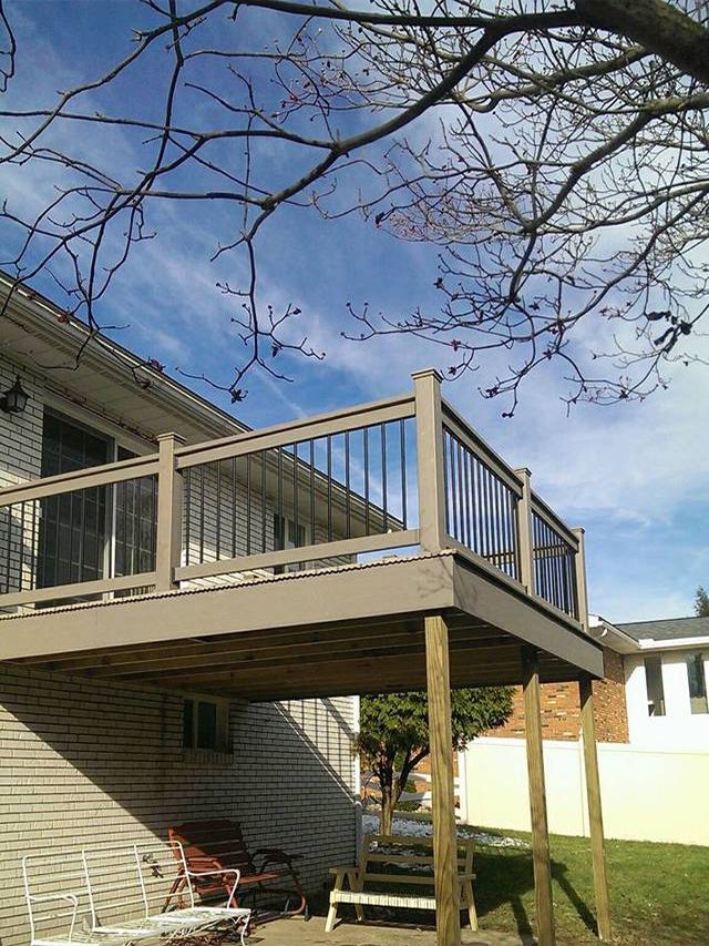 Raised wooden deck attached to a house, with bare tree branches overhead and a grassy yard below
