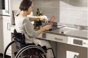 Person in a wheelchair preparing food at a kitchen counter and sink.