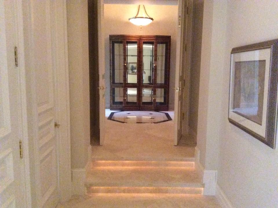 Hallway with two steps and a cabinet at the end, beige walls and floors, and a painting on the right.