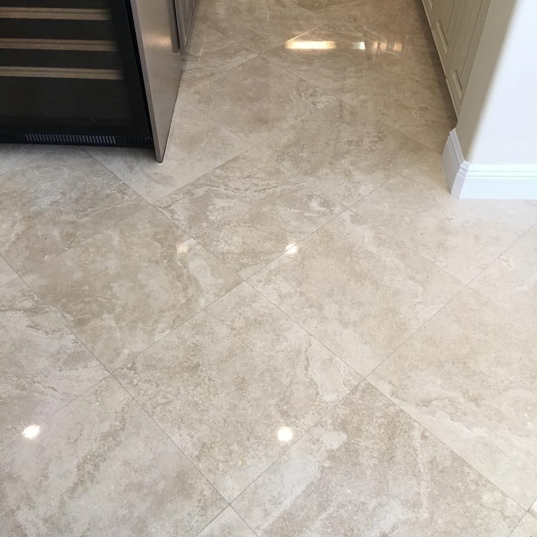 Beige marble tile floor next to a dark appliance, lit by overhead light.