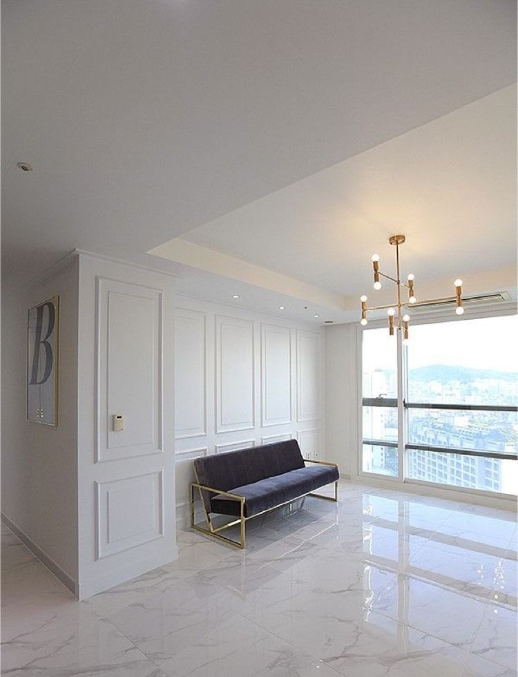 Living room with white walls, gray sofa, gold accents, and a large window with city view.
