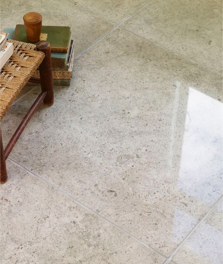 Close-up of speckled light gray floor tiles; small wooden bench with books and cup on it.