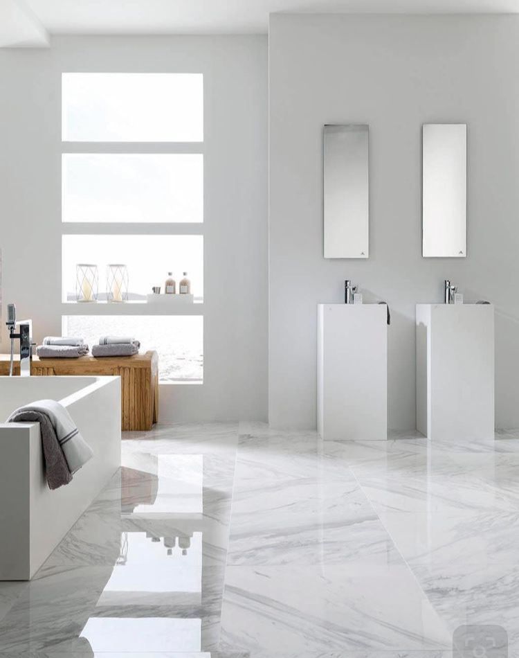 Modern white bathroom with marble floors, two pedestal sinks, and rectangular mirrors.