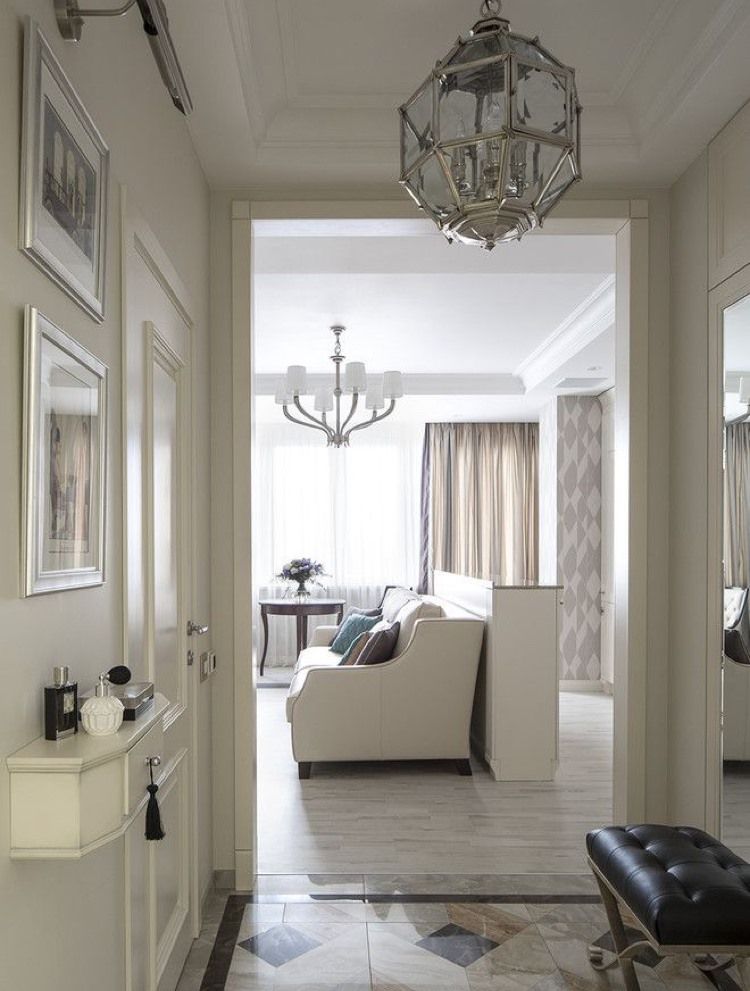Hallway leading to a living room with white walls, patterned floor, and crystal chandeliers.