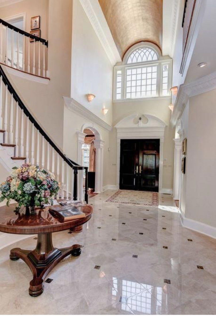 Elegant foyer with a marble floor, curved staircase, and large arched window.