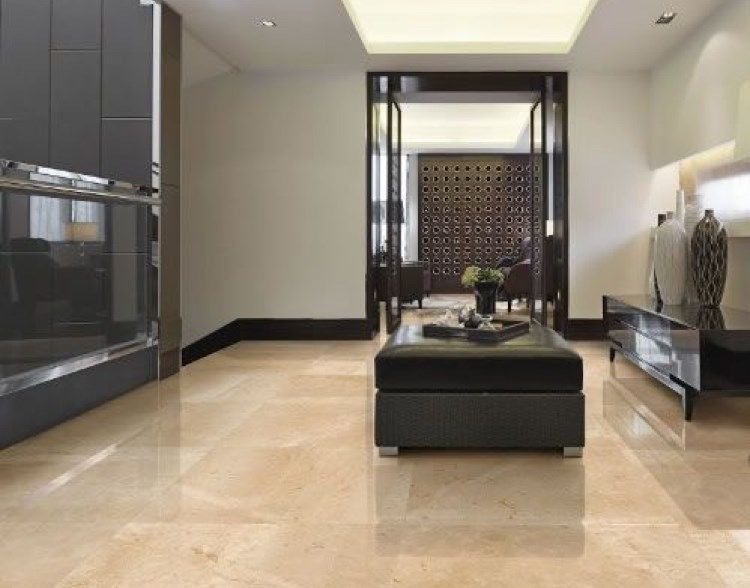 A modern, beige-tiled interior with dark trim, a black ottoman, and an open doorway to another room.