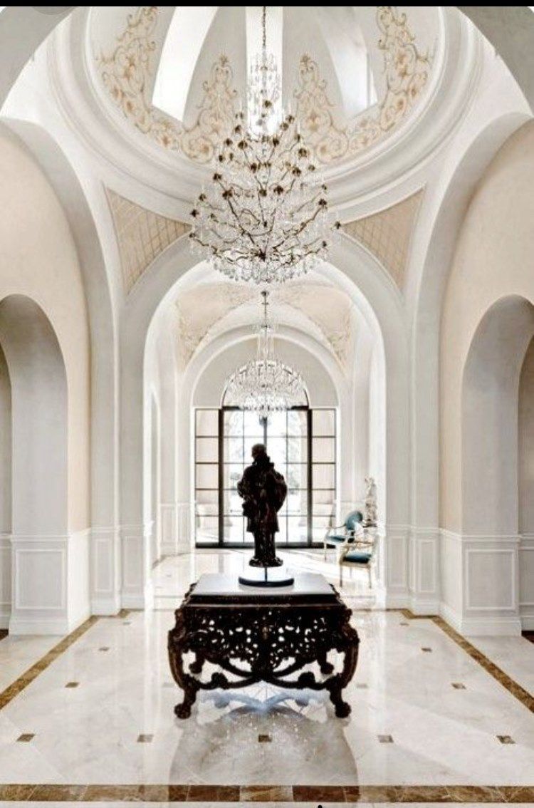 Elegant arched hallway with marble floors, chandelier, and a decorative table with a statue.