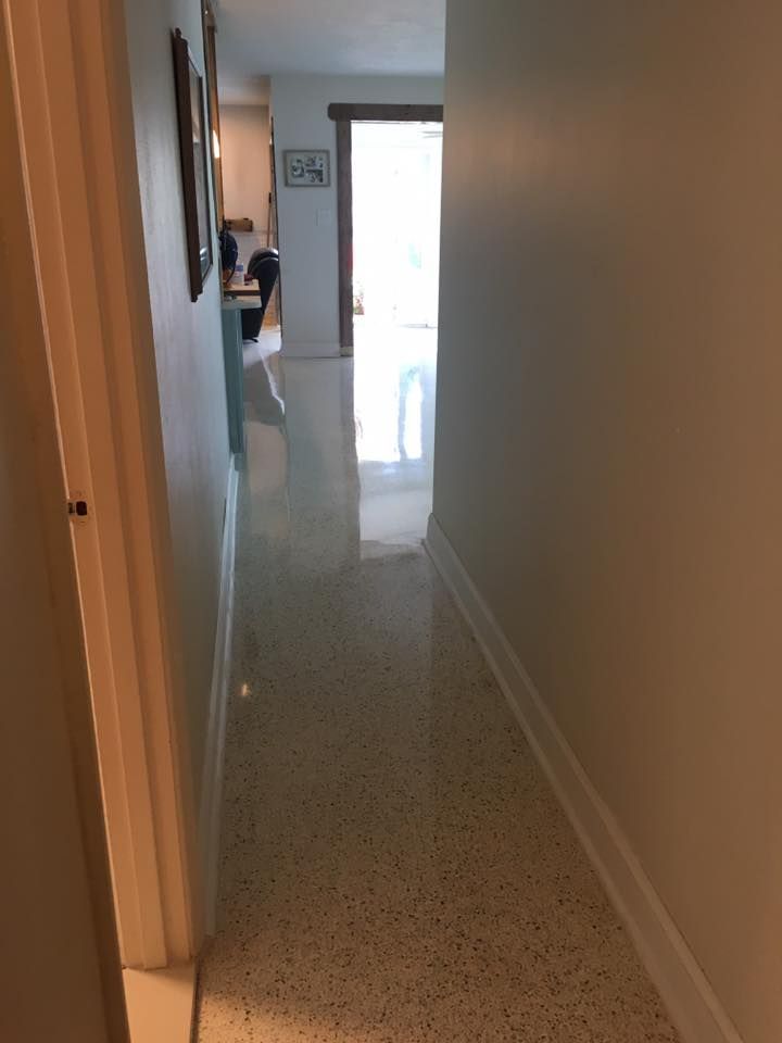 Narrow hallway with polished concrete floor, leading to a bright doorway. White walls and trim.